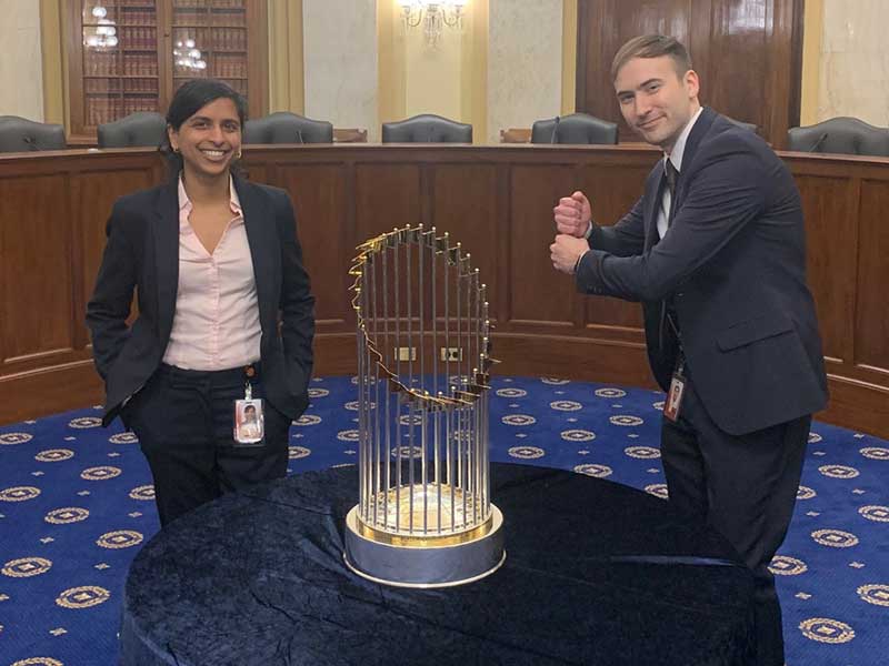 Kyle Robb and a fellow staffer standing with the 2019 World Series trophy in the state house