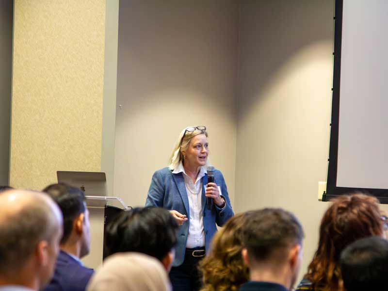 Keynote speaker Cynthia Dowd smiles up at the screen while giving a presentation to an audience in a lecture hall during 2025 Research Day.