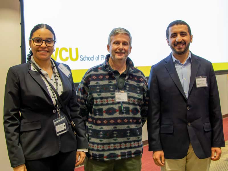 Award winners Cimone Richardson and Hamdan Albukhaytan stand on either side of past chair Doug Sweet, Ph.D., at the front of a lecture hall on Research Day.