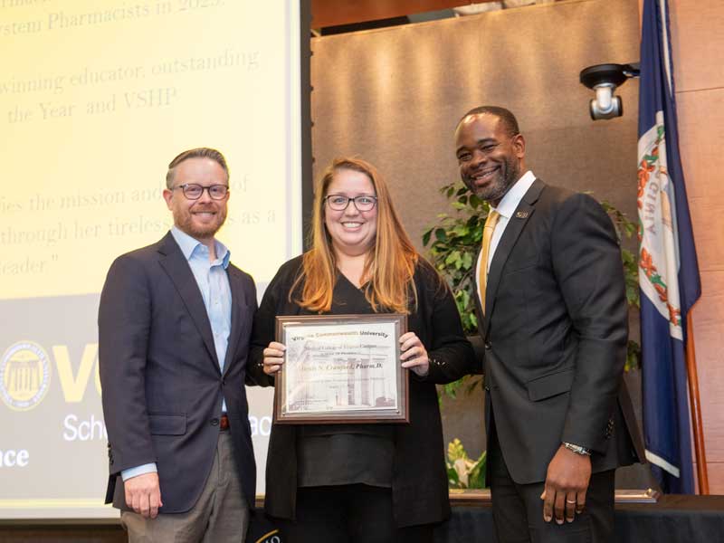 Standing between chair Dave Dixon and Dean K.C. Ogbonna, Alexis Crawford holds a plaque following her promotion