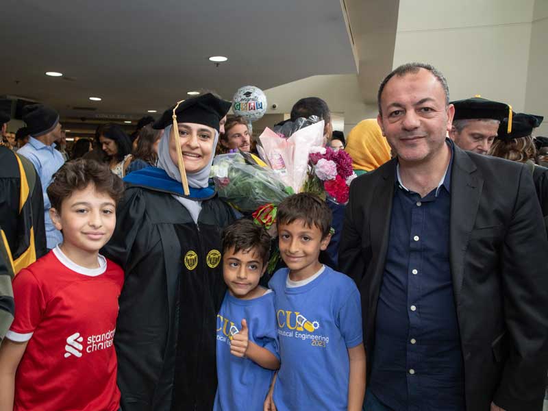 Recent pharmaceutical engineering graduate Asma Al-Terawi, Ph.D., in her doctoral tam, hood and gown poses for a family photo with her husband and their three sons after the VCU School of Pharmacy Hooding and Diploma Ceremony on May 9, 2025.