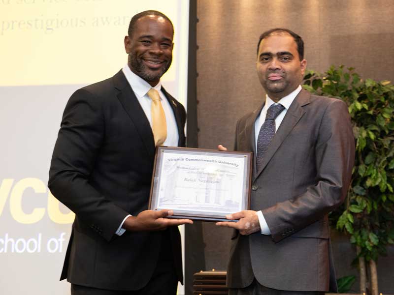 Standing next to Dean K.C. Ogbonna, Balaji Nagarajan accepts the Exceptional Customer Service Award