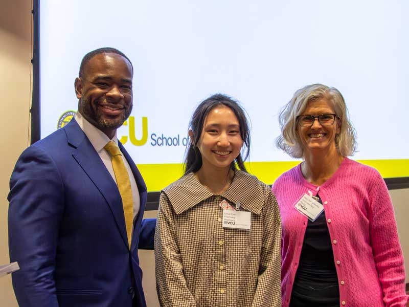 Dean K.C. Ogbonna and Associate Dean Mary Peace McRae stand on either side of Pharm.D. award winner Erica Eom, at the front of a lecture hall on Research Day.