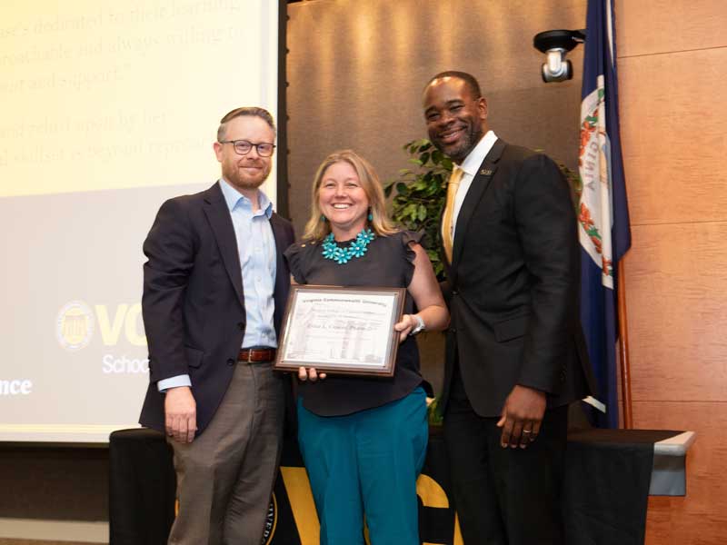 Standing between chair Dave Dixon and Dean K.C. Ogbonna, Ericka Crouse holds a plaque following her promotion