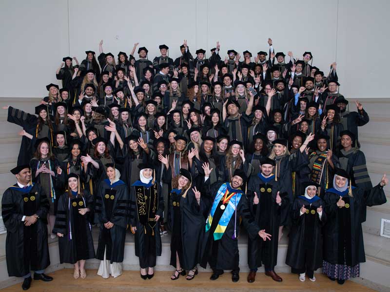 More than 100 members of the VCU School of Pharmacy Class of 2025 in academic regalia (doctoral tams, hoods and gowns) gather on risers for a fun photo of them celebrating their graduation