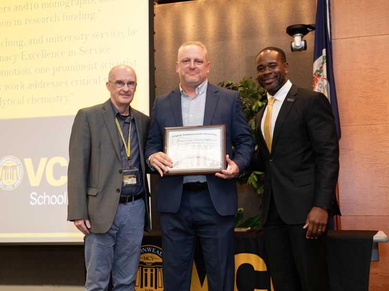 Standing between interim chair Michael Hindle and Dean K.C. Ogbonna, Matthew Halquist holds a plaque following his promotion