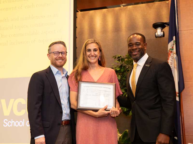 Standing between chair Dave Dixon and Dean K.C. Ogbonna, Nicole Omecene holds a plaque following her promotion