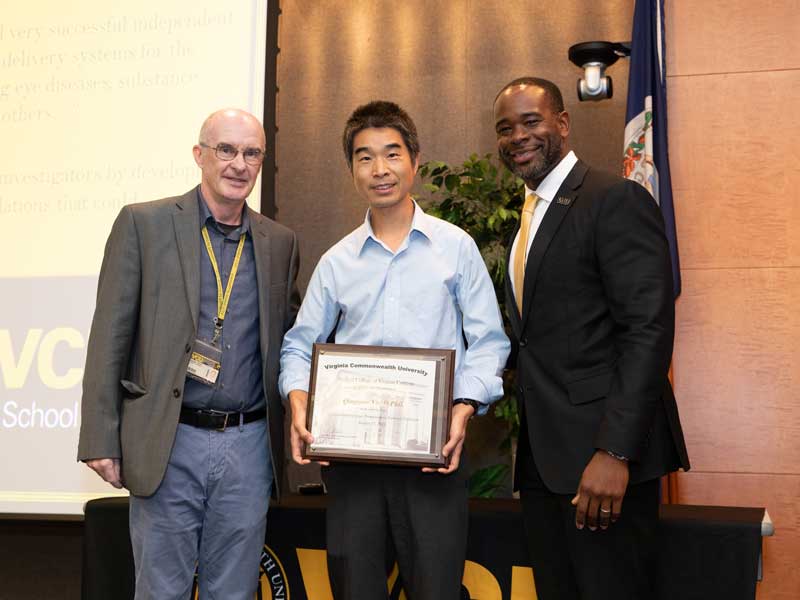 Standing between interim chair Michael Hindle and Dean K.C. Ogbonna, Qingguo Xu holds a plaque following his promotion