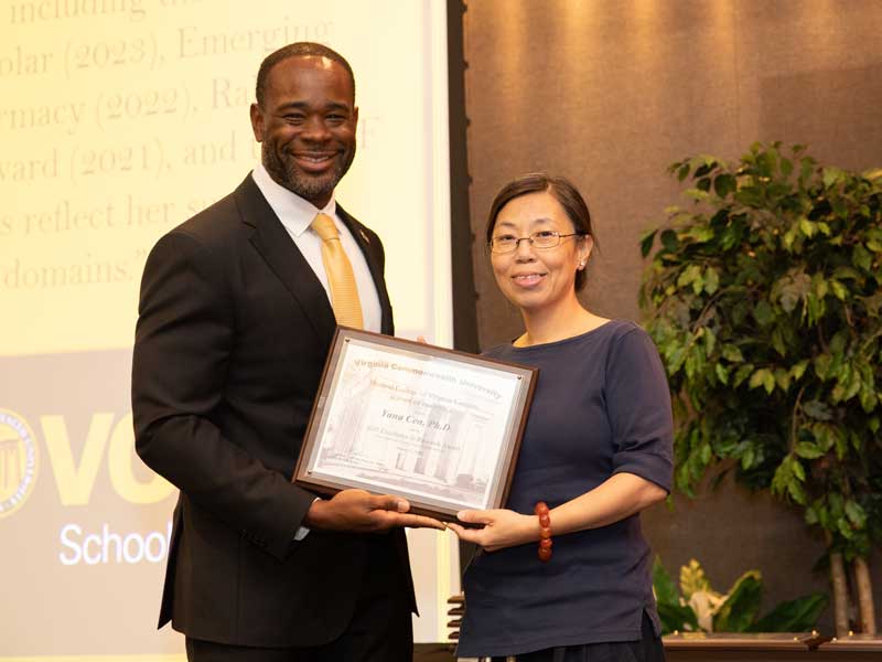 Standing next to Dean K.C. Ogbonna, Yana Cen accepts the Excellence in Research Award